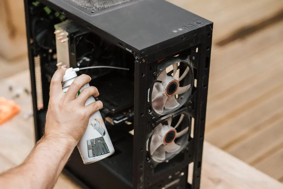 Crop anonymous male with compressed air can removing dust from computer system unit